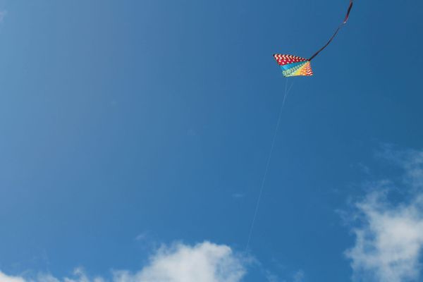 Blue sky with a brightly-colored triangular kite in the upper left corner of image. Clouds are present in the lower part of image.