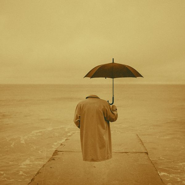 Invisible human wearing a trench coat and holding an umbrella standing at the edge of ocean. 
