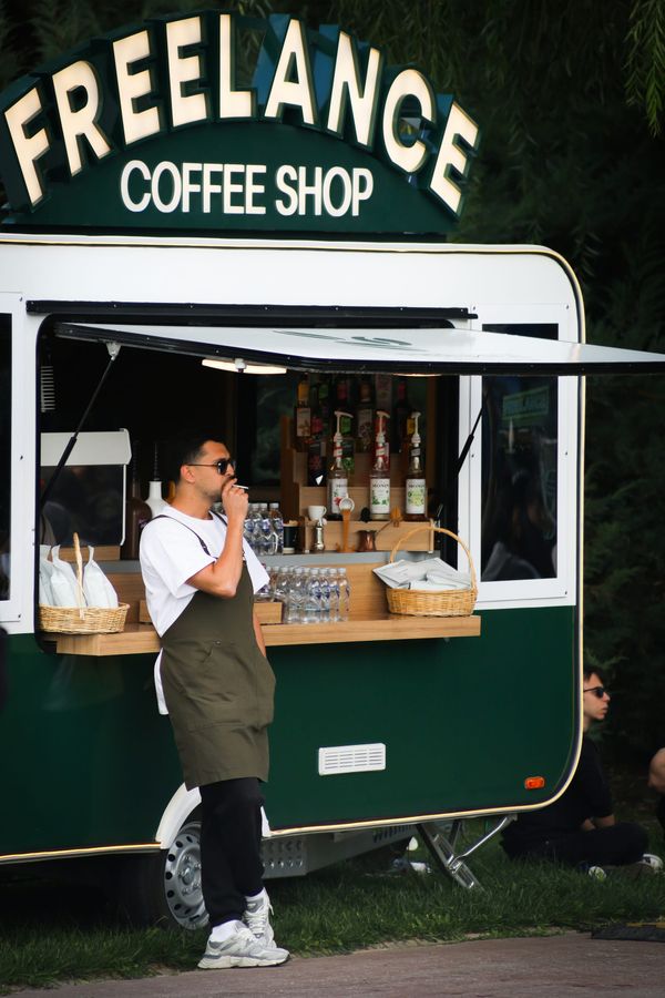 Owner of the Freelance Coffee Shop trailer leaning again his trailer smoking a cigarette.