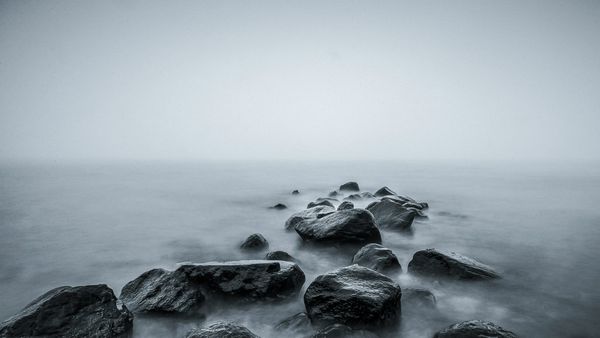 Large boulder outcropping extending into a gray and foggy body of water. The boulders are also gray in color.