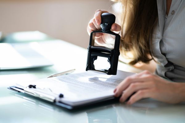 Image of a woman stamping a document on a clipboard with large hand stamp.