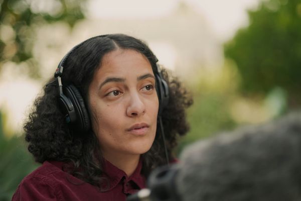 Woman wearing headset holding a microphone recording outside. Presumbably a field reporter.
