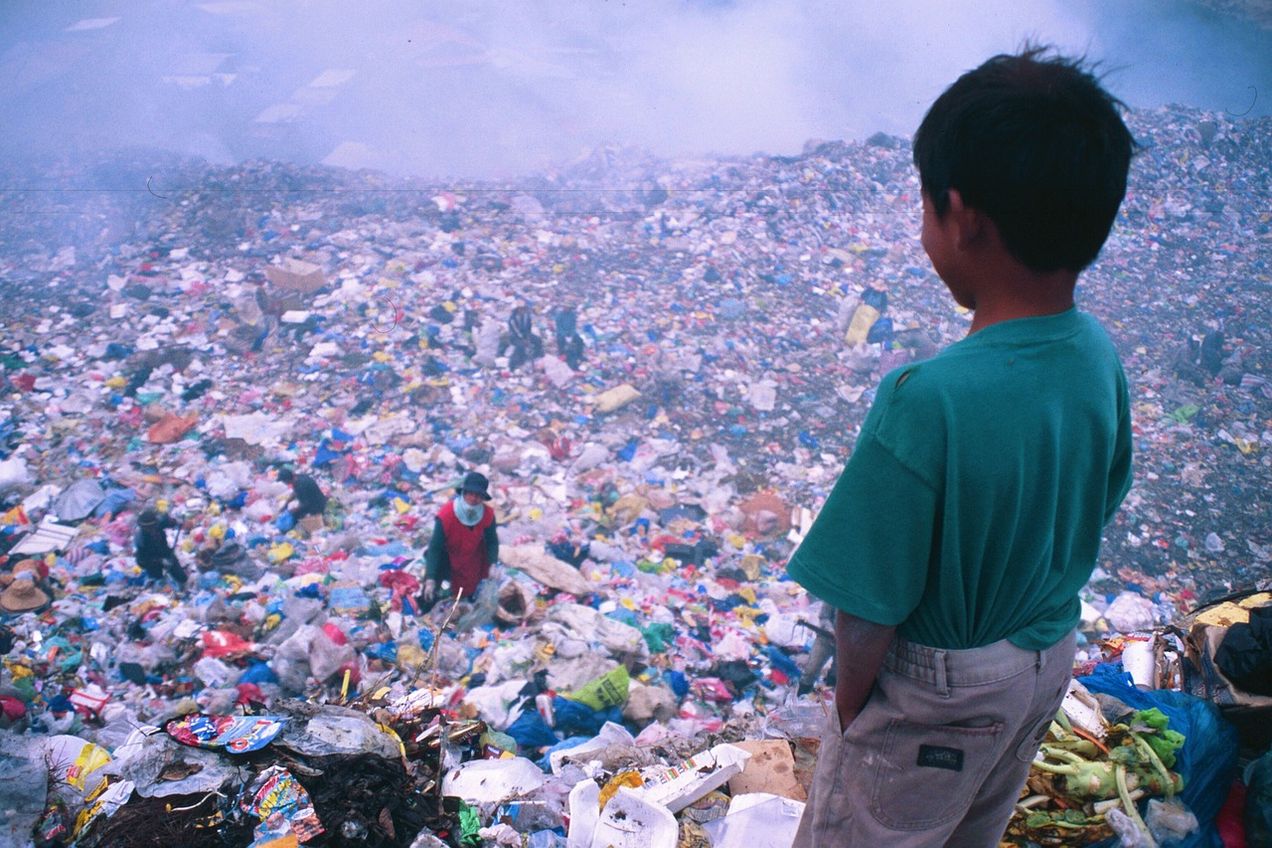A boy looks down at a huge, sprawling garbage dump | Too many people
