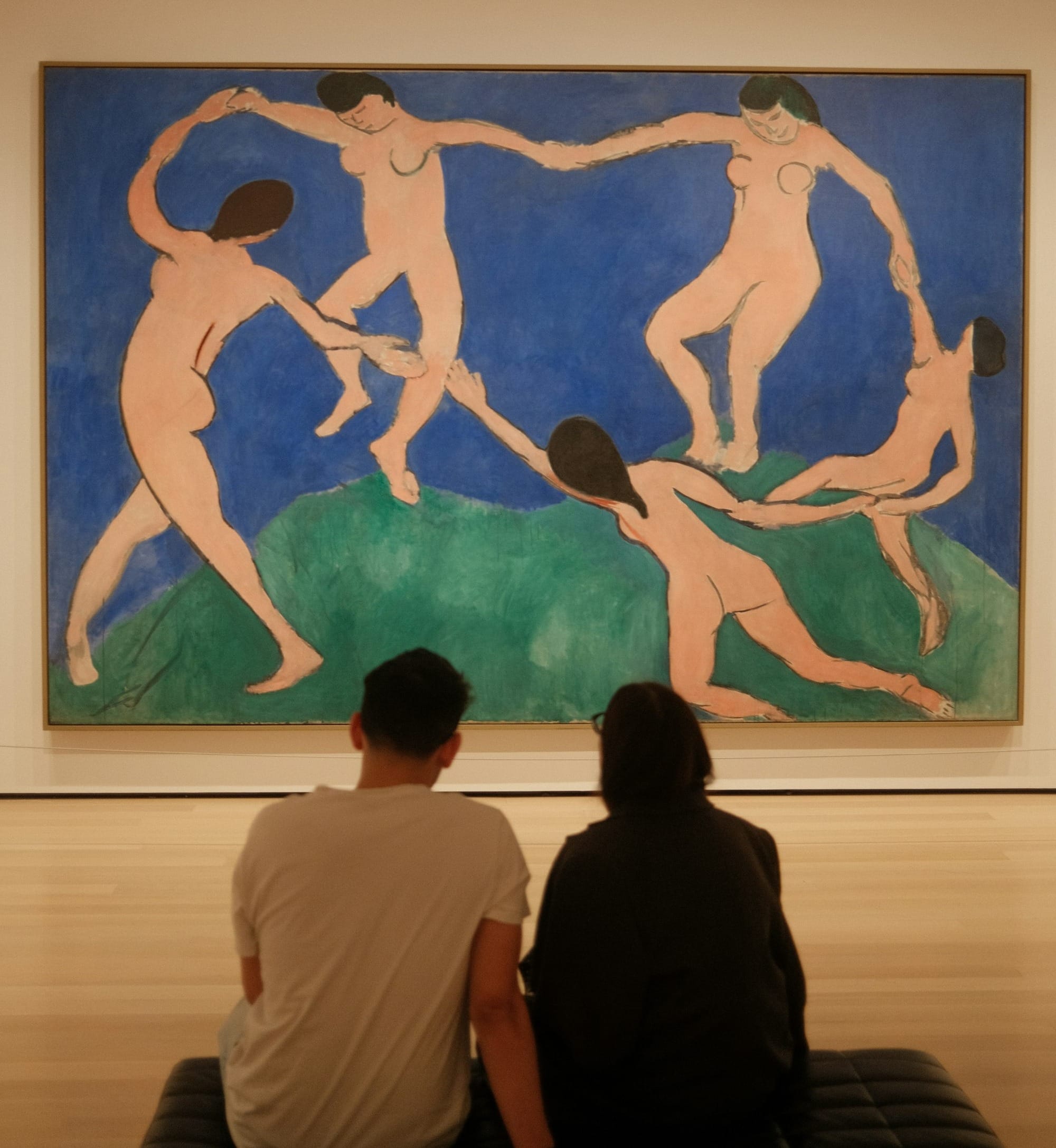 two people sitting on a bench in front of a painting