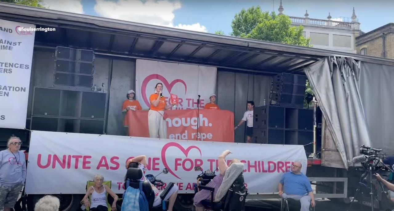 Enough ambassador Beaver Meadows on stage at 'For the Children' rally, in front of an Enough banner.