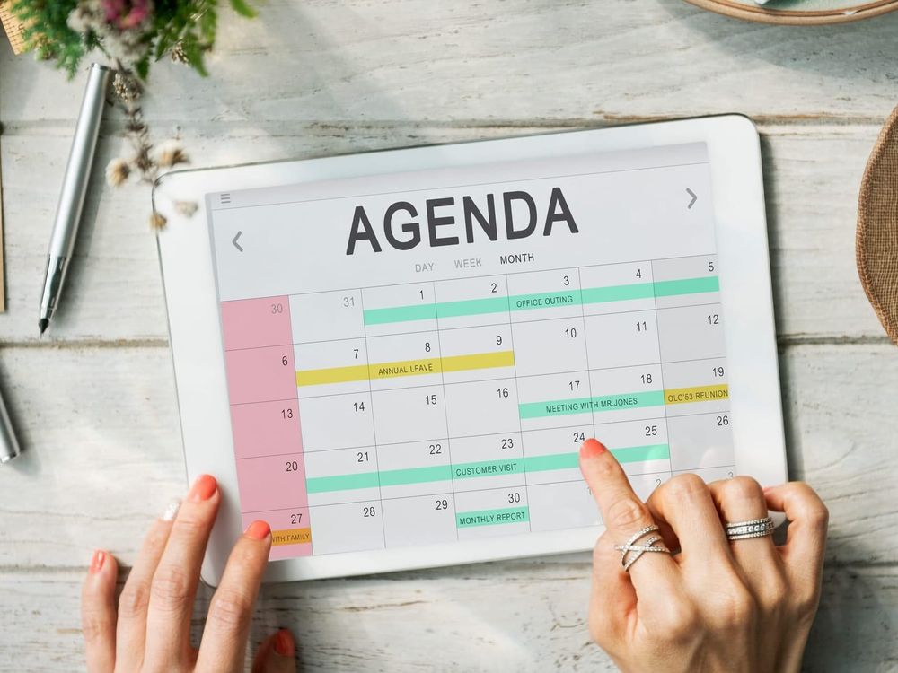 Na imagem: mãos seguram um tablet com agenda aberta e compromissos marcados