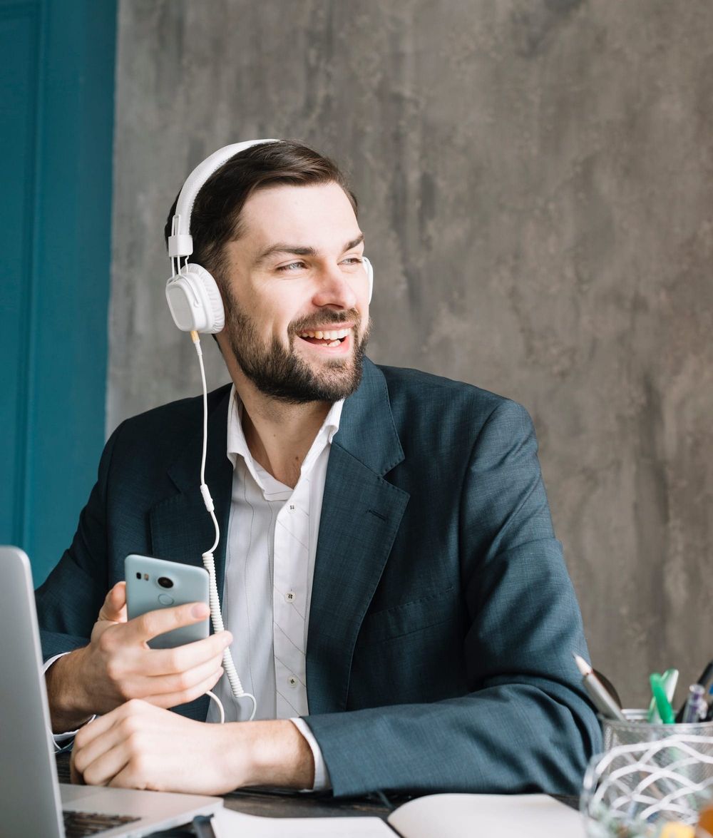 Na foto: homem de fone de ouvido está descontraído com o celular na mão