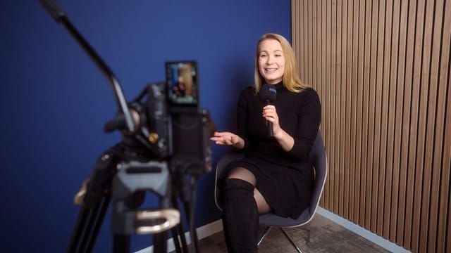 Eine Frau in einem modernen Setting, die vor einer Kamera sitzt und in ein Mikrofon spricht – ein professioneller Moment in d