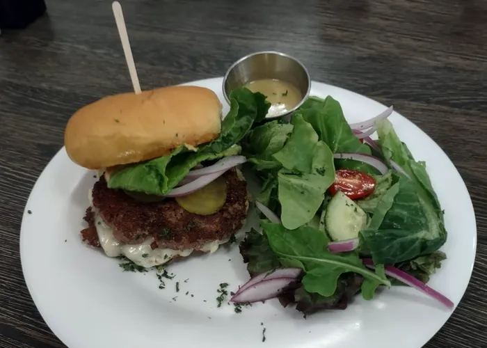 a hamburger with bun, lettuce, tomato, and a side of sauce on a white plate