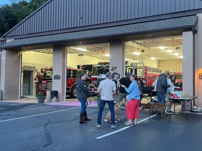 folks gathered around a grill by the fire trucks at the station