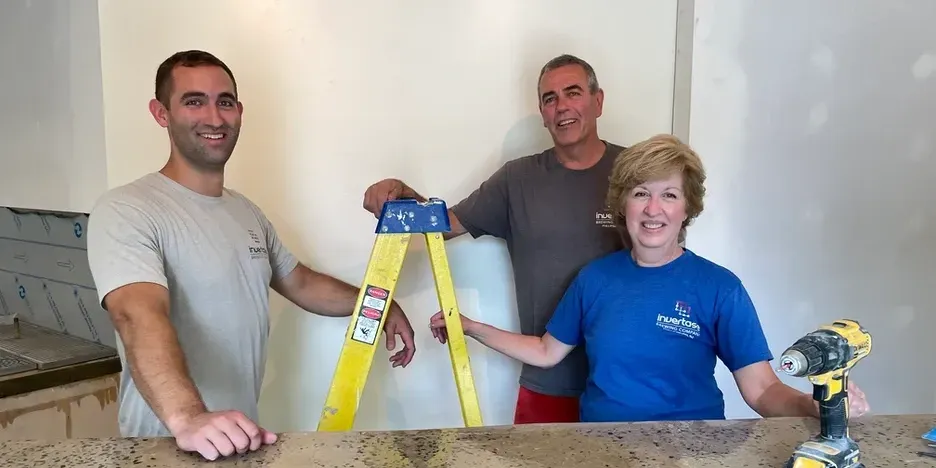an adult son and his parents stand near a ladder in their soon-to-open brewery