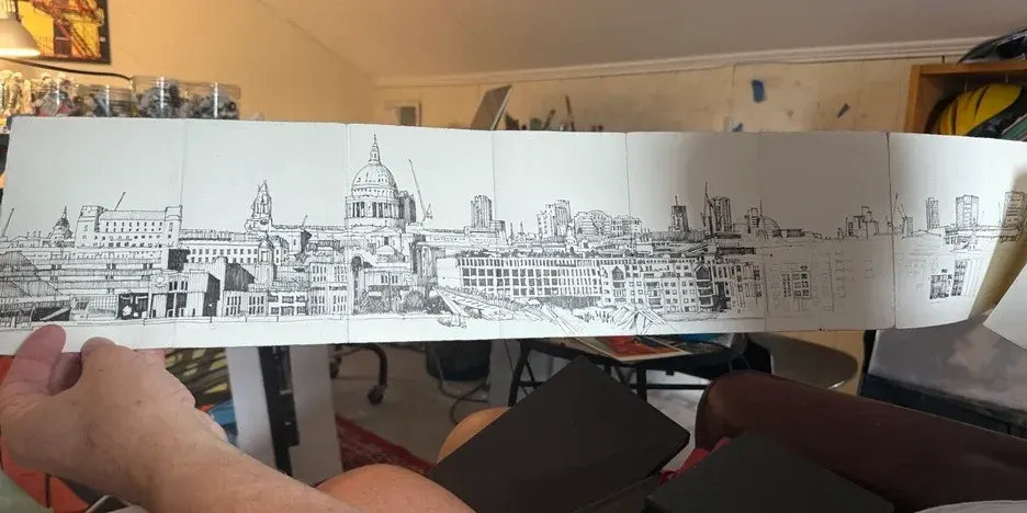 hands holding a long, unfolded string papers with a drawing of a cityscape on it