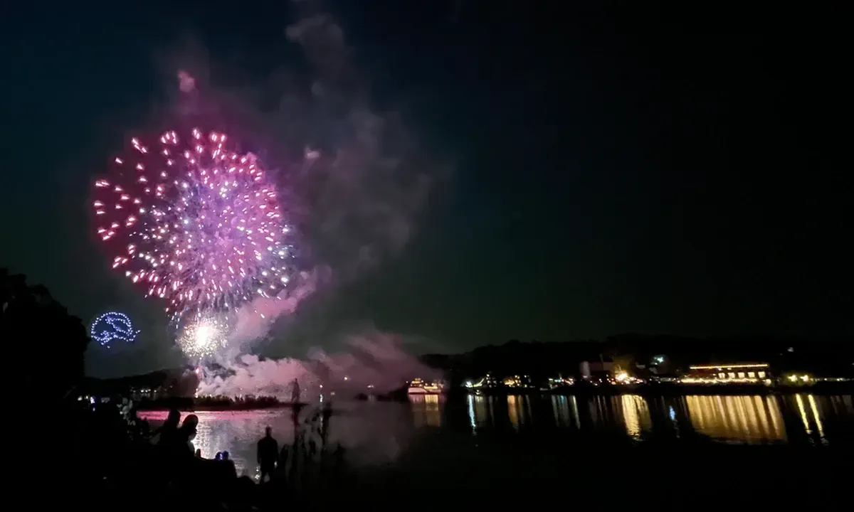 a purple firework blast hovers over the dark river at night