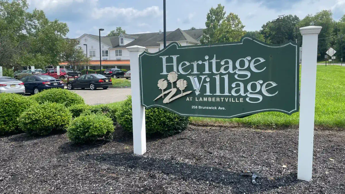 a wood sign that reads "Heritage Village at Lambertville" with an apartment building in the background