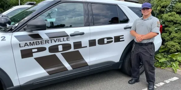 a smiling young man in uniform, standing next to a police cruiser