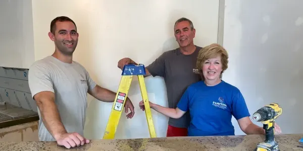 an adult son and his parents stand near a ladder in their soon-to-open brewery