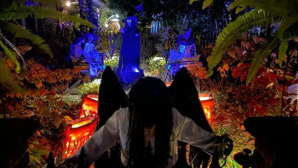 a demon angel stands before a coven of witches and skeletons in a front yard
