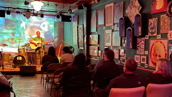 a solo performer plays guitar and sings on stage before a live audience