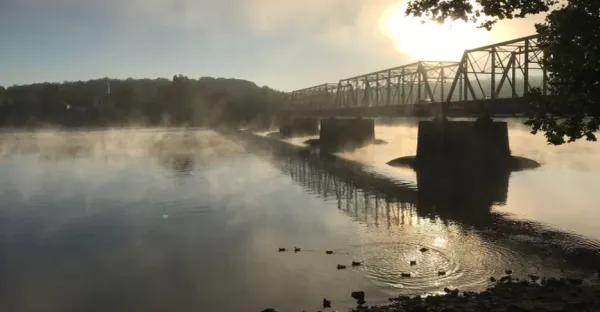 the misty morning Delaware River with a war sun shining behind the Lambertville/New Hope Bridge
