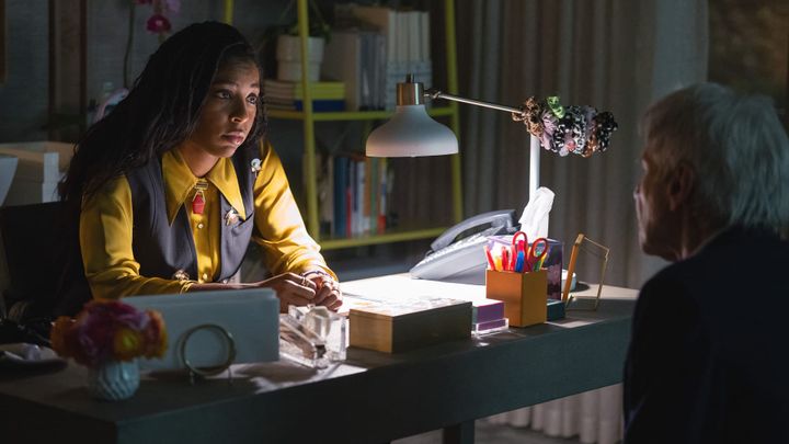 Jessica Williams sits at desk, looking speaking with Harrison Ford