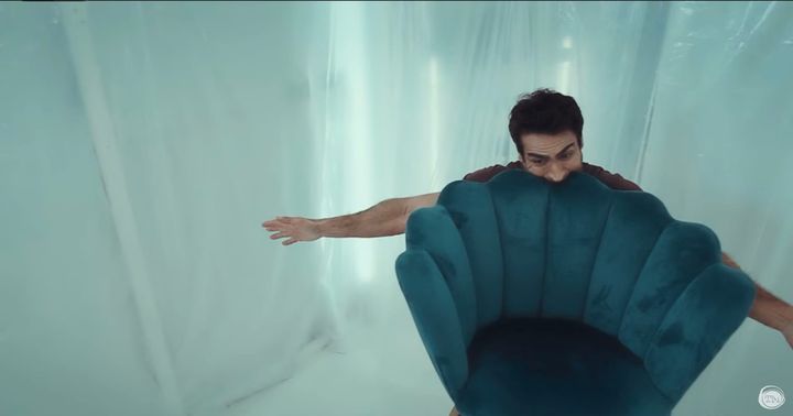 Kumail Nanjiani with a chair in his mouth.