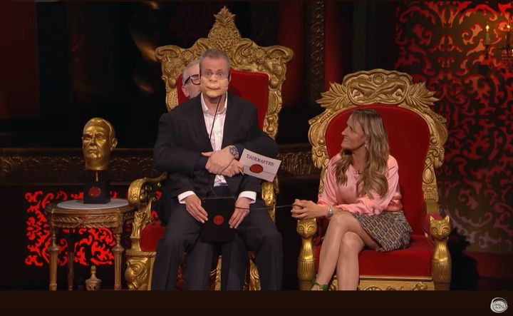 Little Alex Horne wears a ventriloquist’s mask and sits on Greg Davies’ lap. Nina Conti sits in the chair next to them.