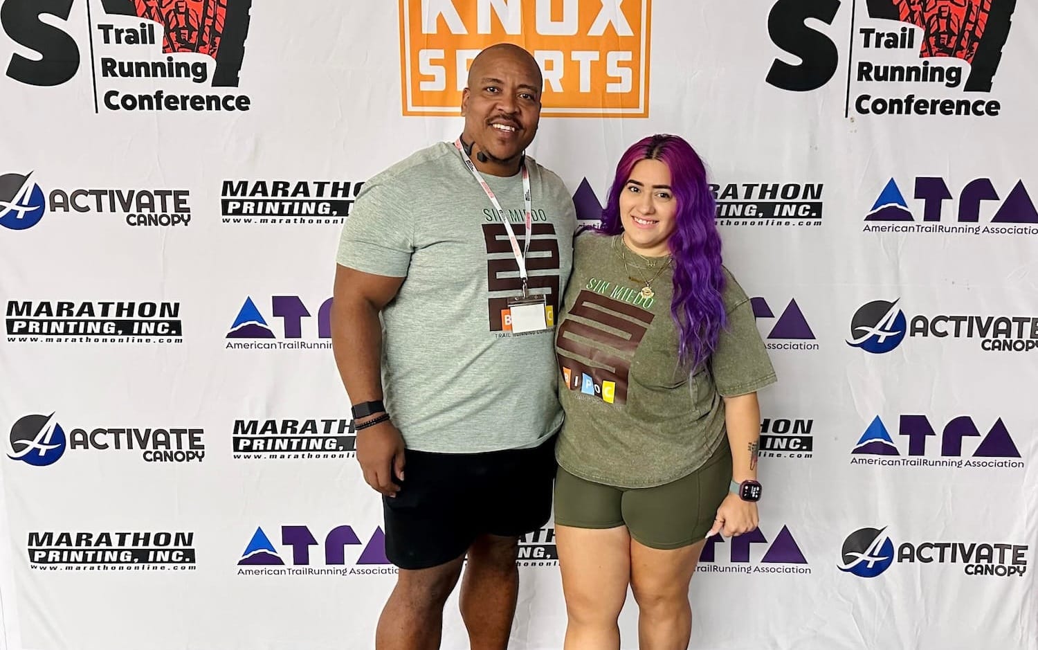 A man and a woman posting for a photo in front of a backdrop with logos on it