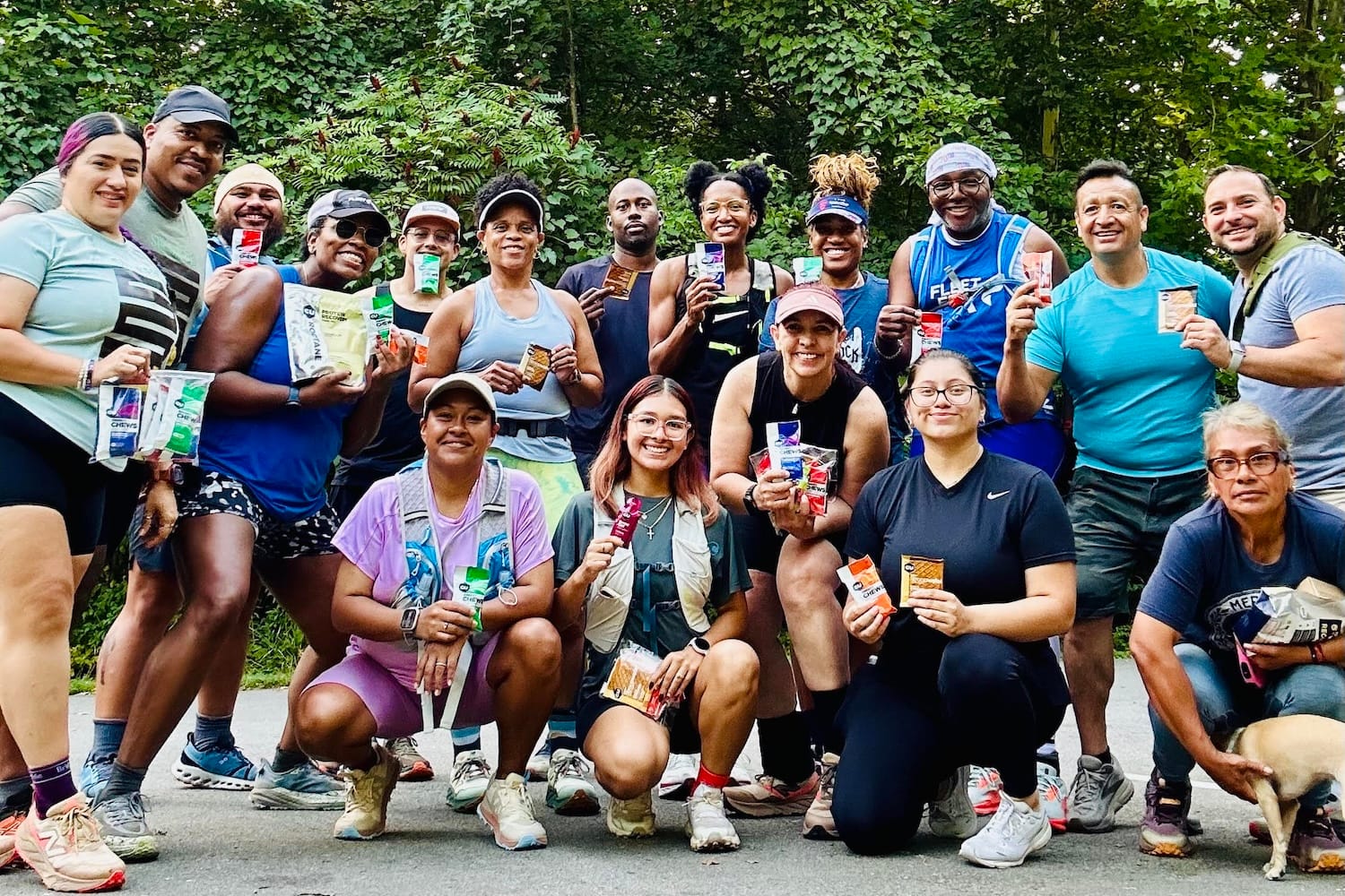 A group of runners posing for a photo outside with green trees in the background