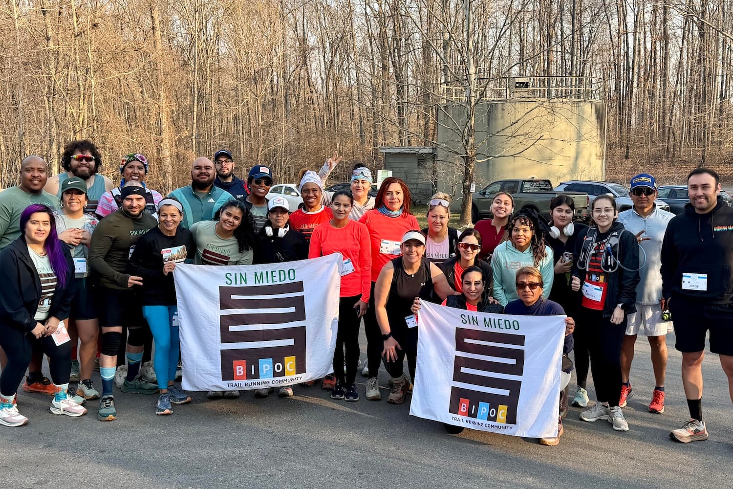 A large group of runners posing with two banners, outdoors with trees without leaves in the background
