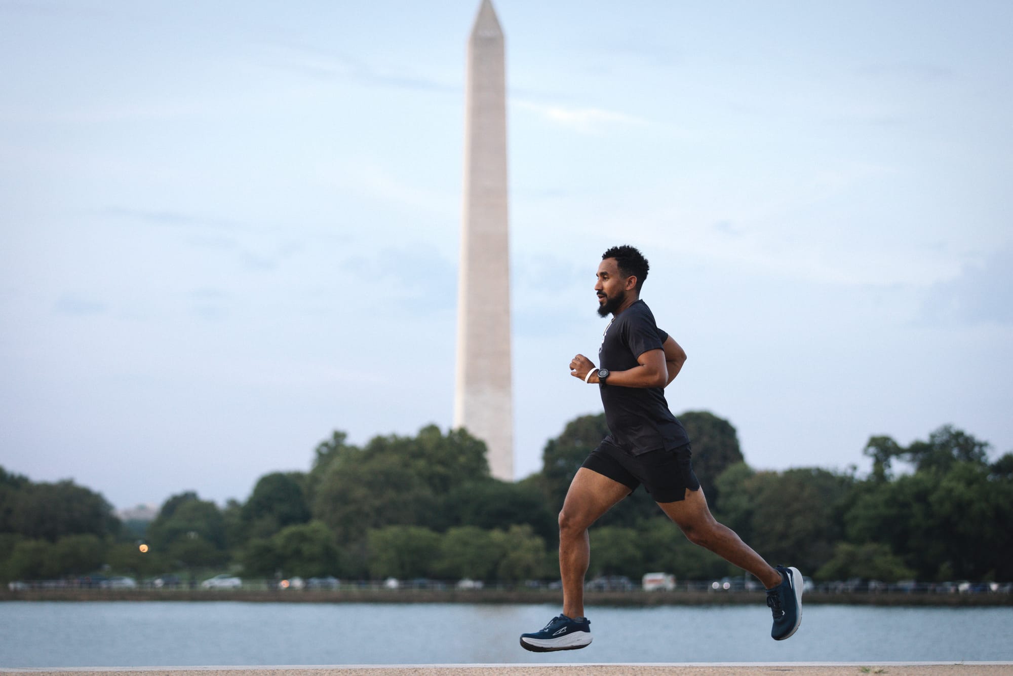 A man running in front of water, green trees, and Washington National Monument