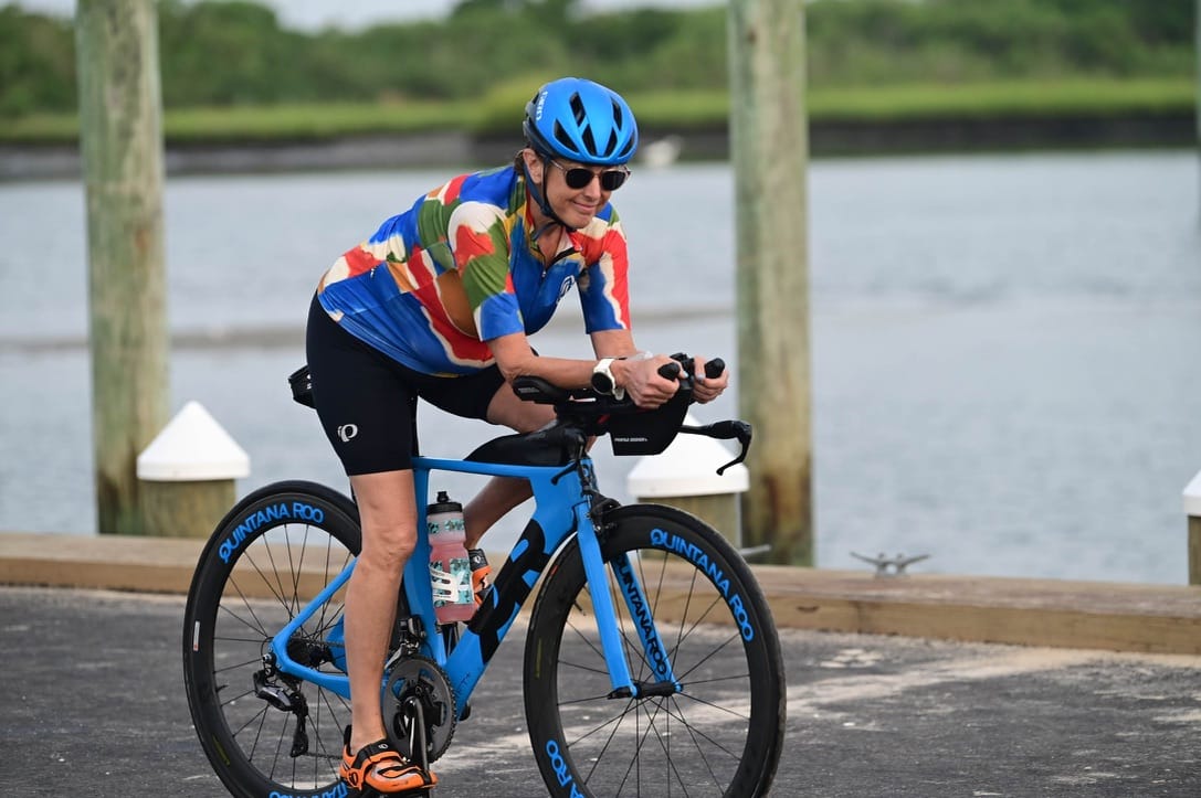 A woman riding a triathlon bike on a paved path with a lake in the background