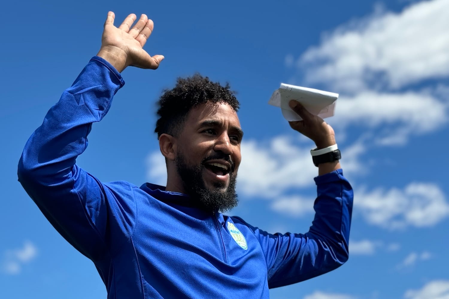 A man in a blue long-sleeve shirt smiling and raising his arms