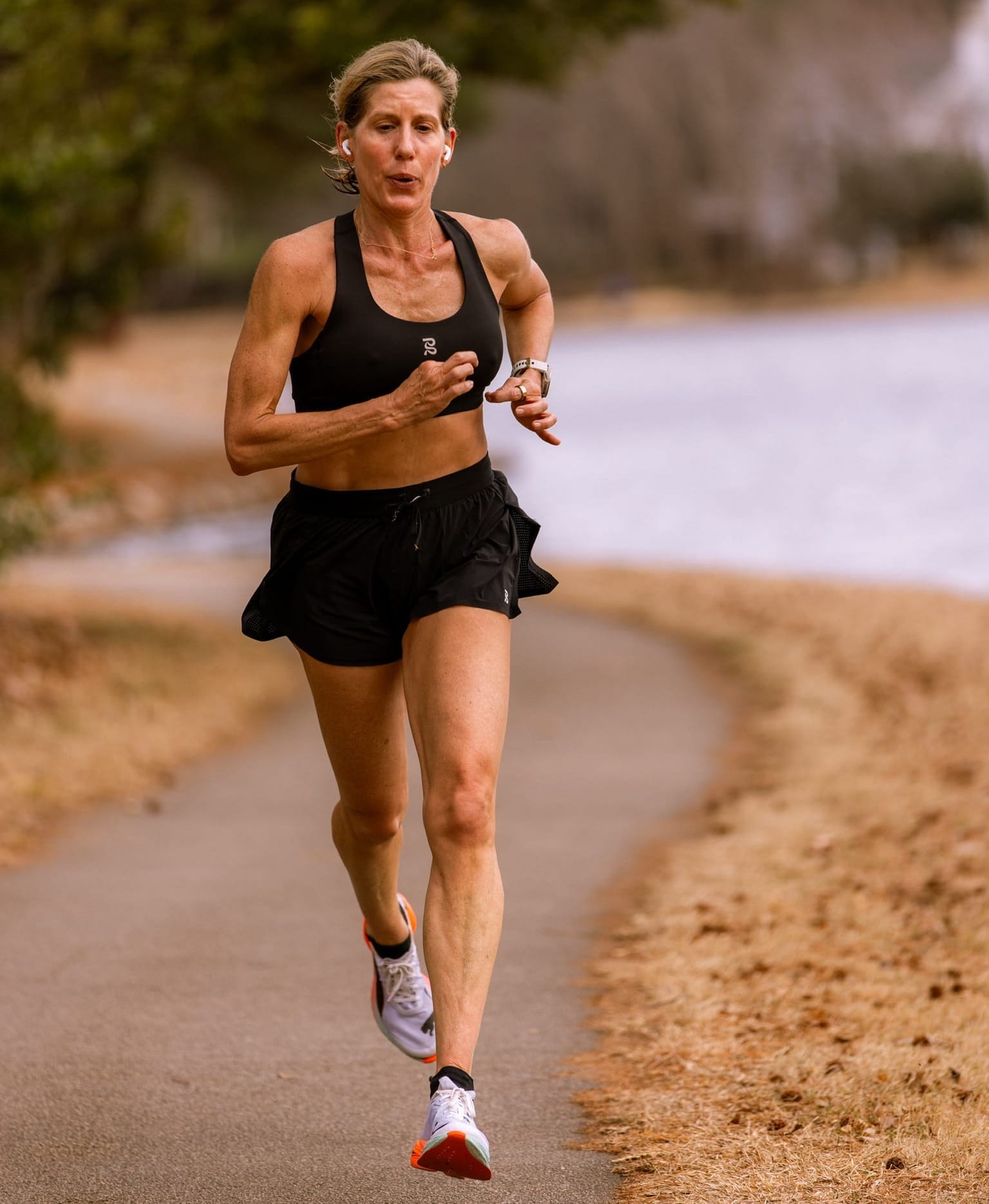 A woman in black running apparel running along a path with a lake in the background