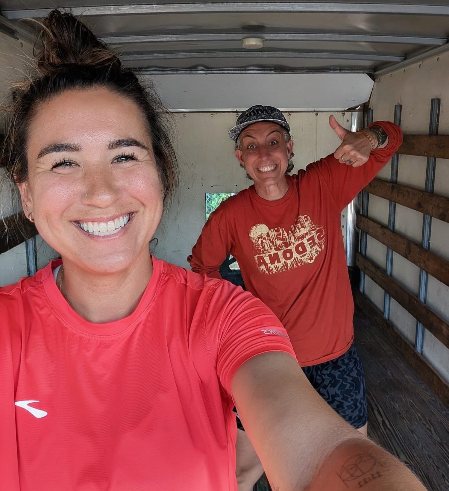 A women taking a selfie inside of a truck with another woman behind her giving a thumbs up