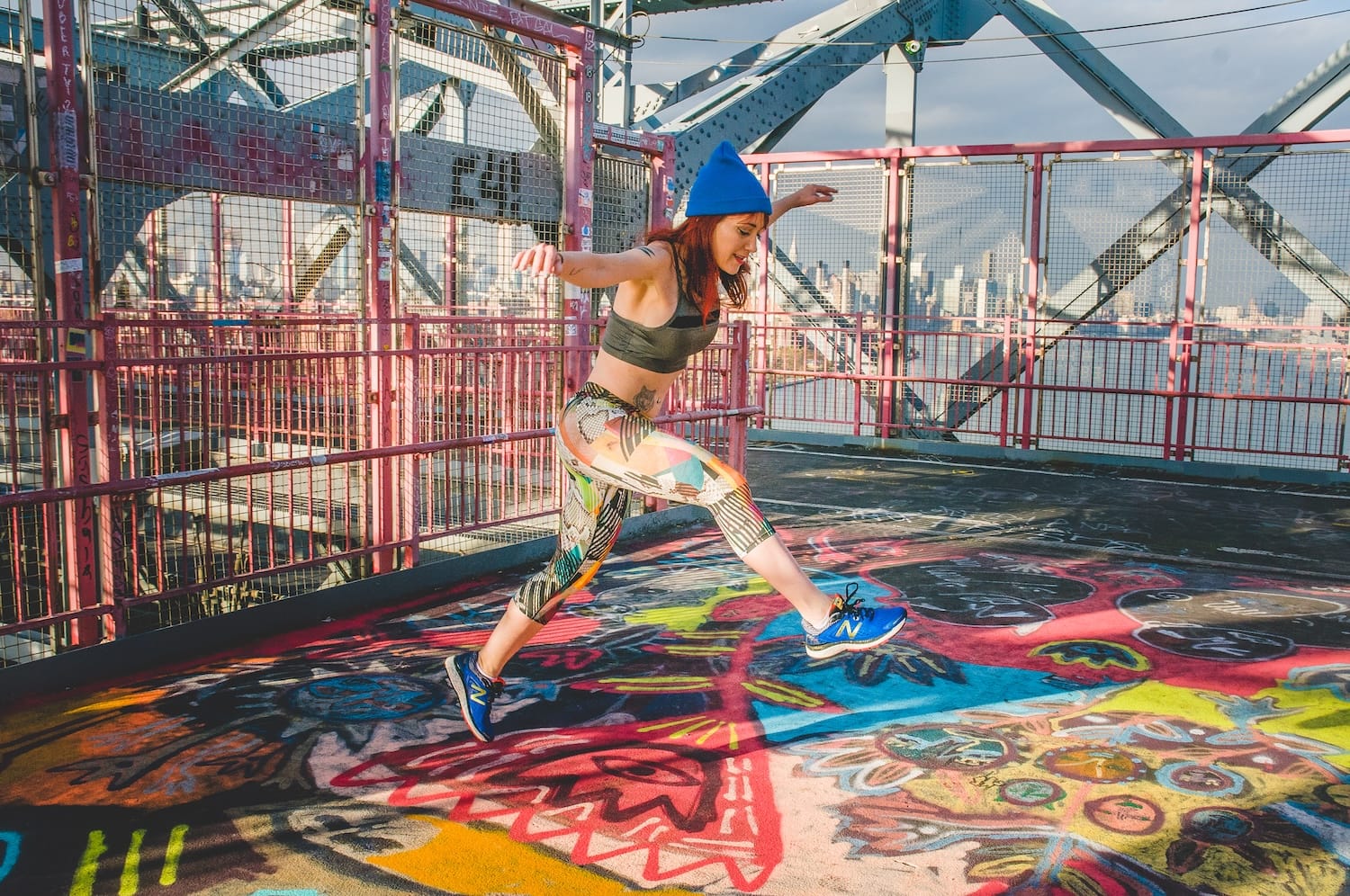 A woman in colorful athletic apparel jumping on a outdoor floor covered in colorful murals