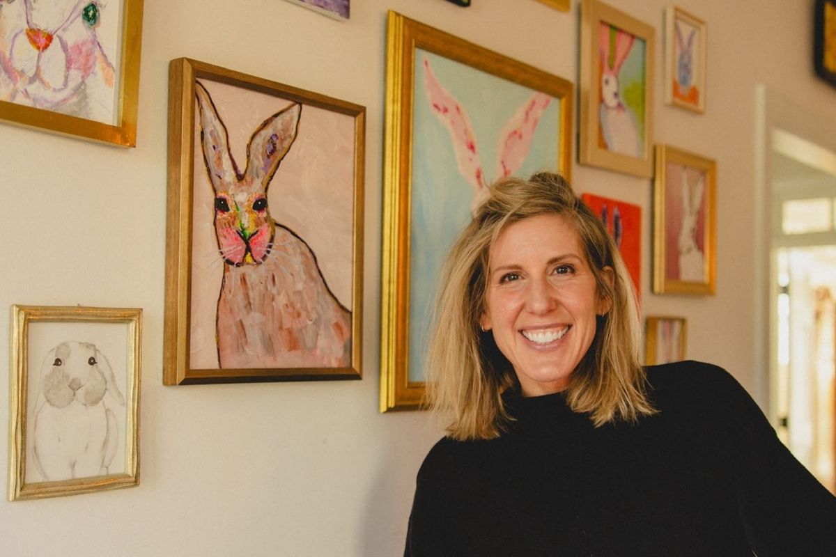 A woman smiling in front of a wall with framed paintings of rabbits