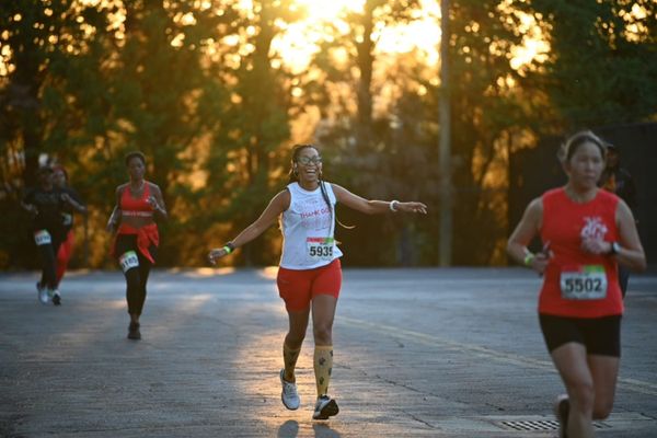 Several women running in a race on a paved road with trees in the background