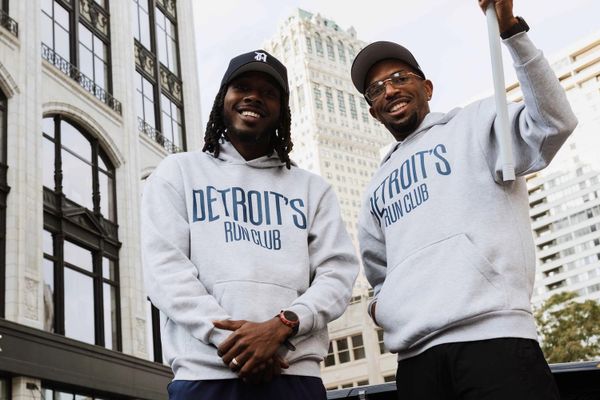 Two men in white sweatshirts and black hats, posing for a photo in front of city buildings