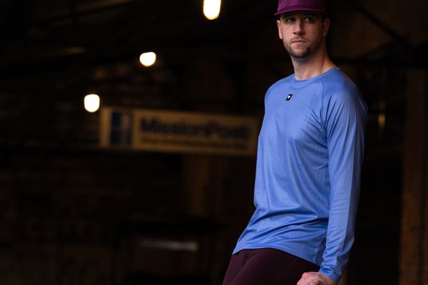 A man standing and looking straight ahead wearing a blue long-sleeve t-shirt
