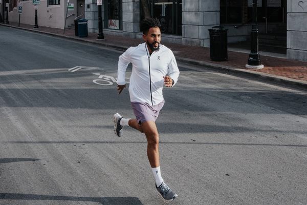 A man in a white zip-up jacket running down a paved street