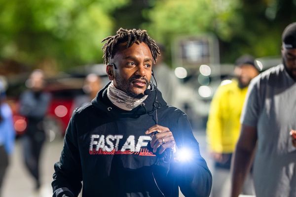 A man in a jacket holding a flashlight outside in the dark with runners around him