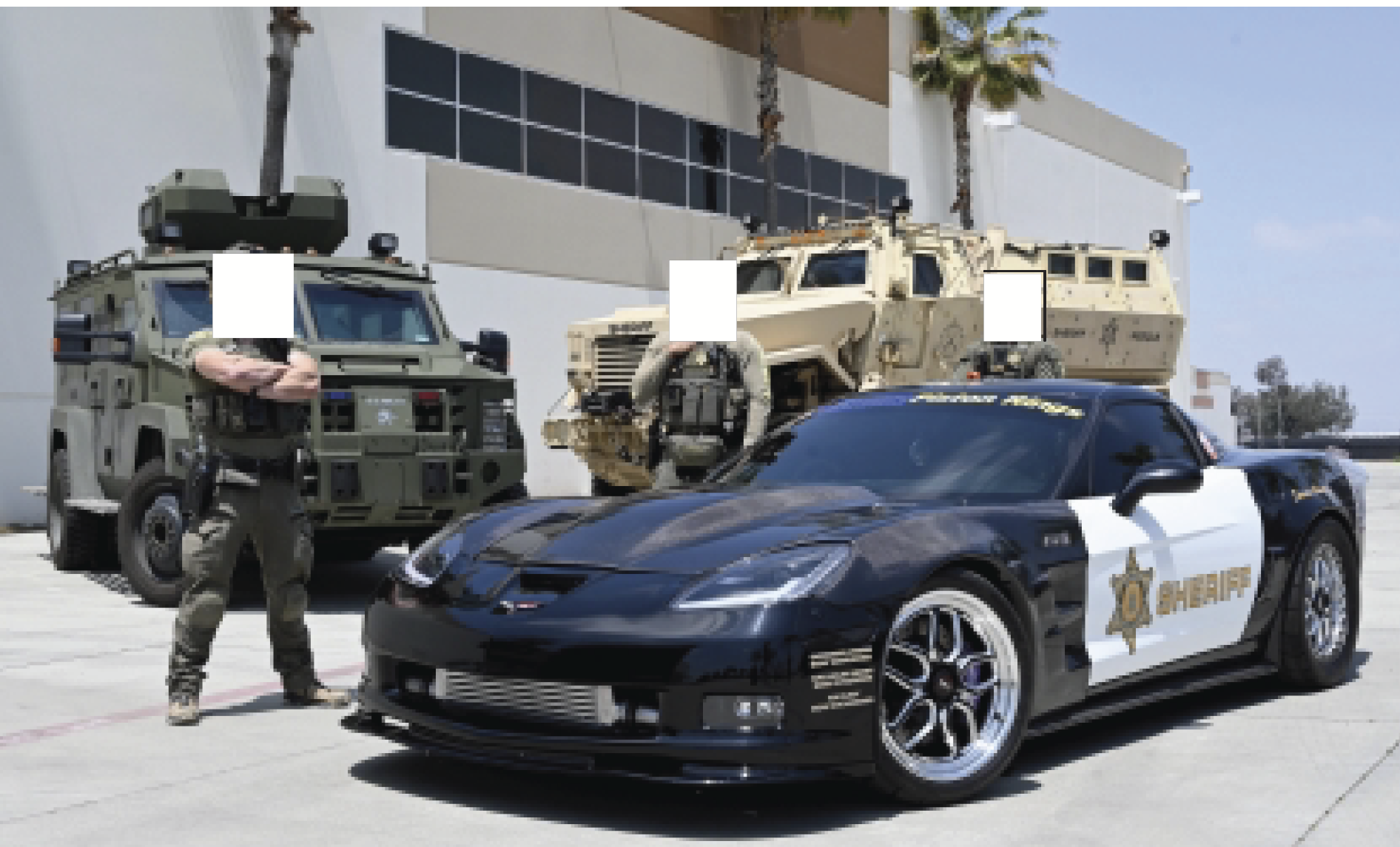 Three Sheriffs with redacted faces stand behind a Corvette drag car with department decals on it. Behind them are two armored vehicles.
