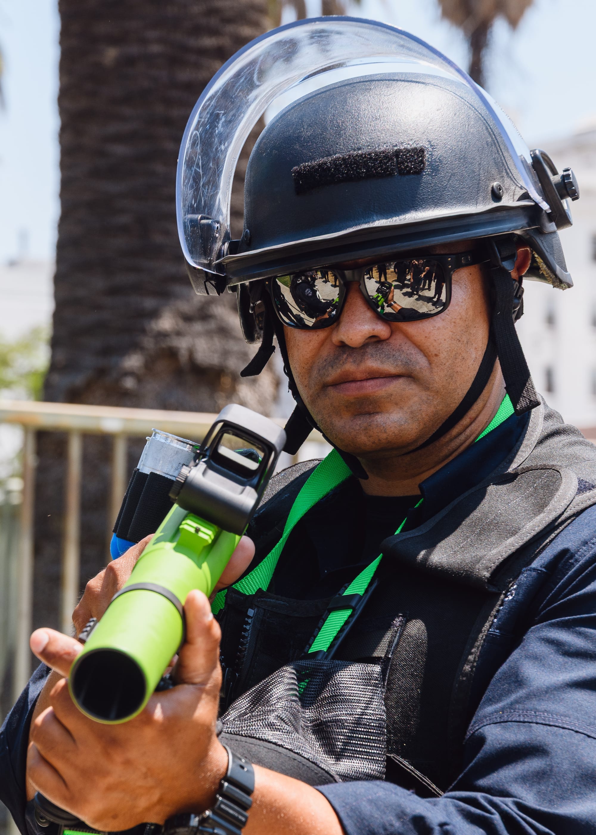 A police officer holding a green gun with riot gear on. 