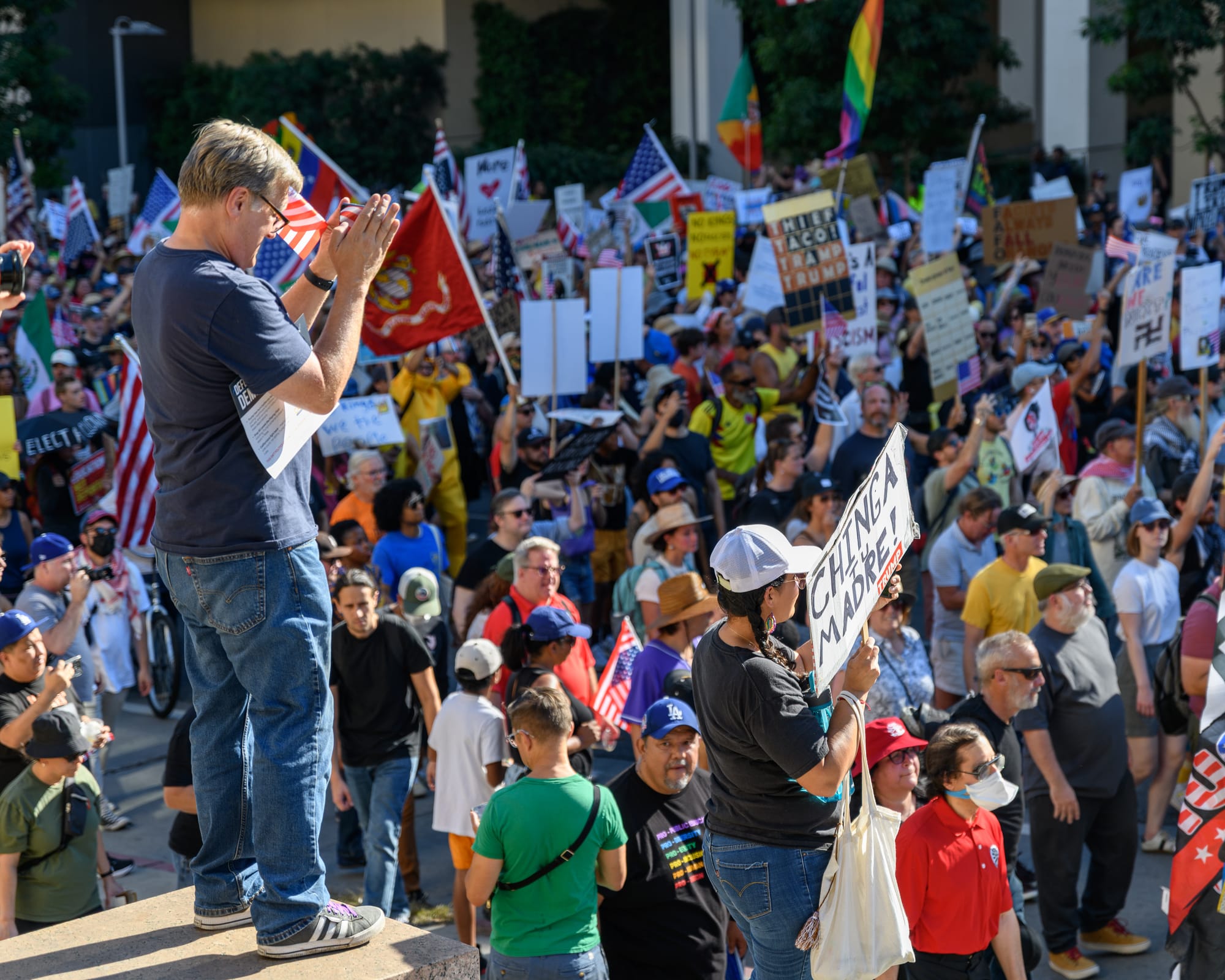 A man photographs a march at the No Kings rally in Los Angeles. The crowd is holding signs and wearing costumes. 