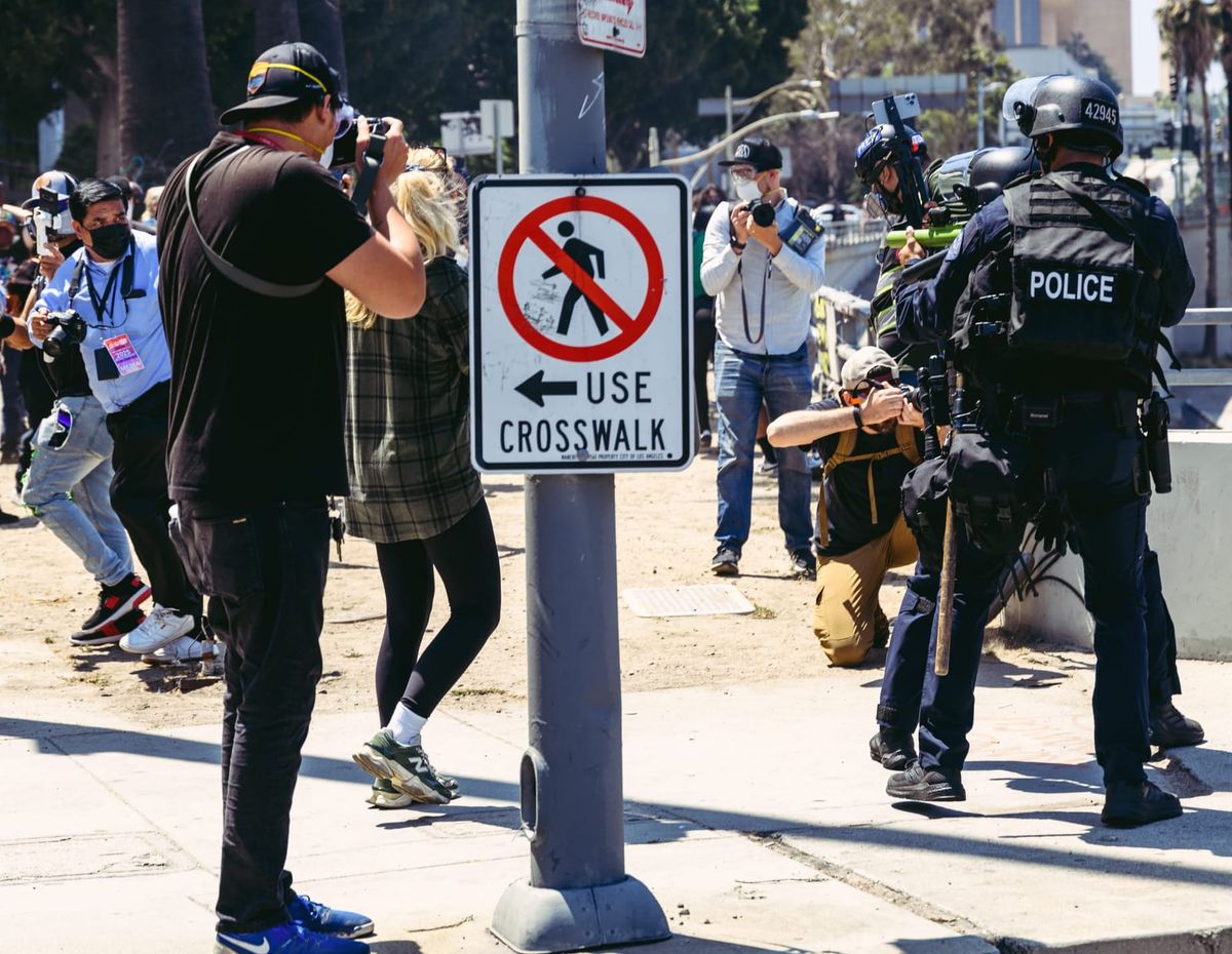 People, including journalists, flee as police officers in riot gear point guns at them.