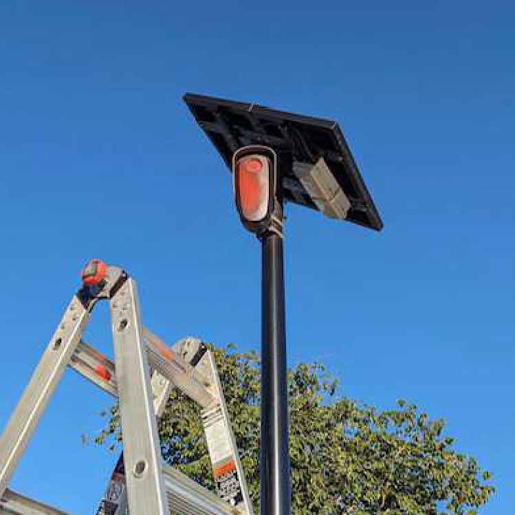 A ladder stands next to a pole with a camera spray painted over and a solar panel on top.