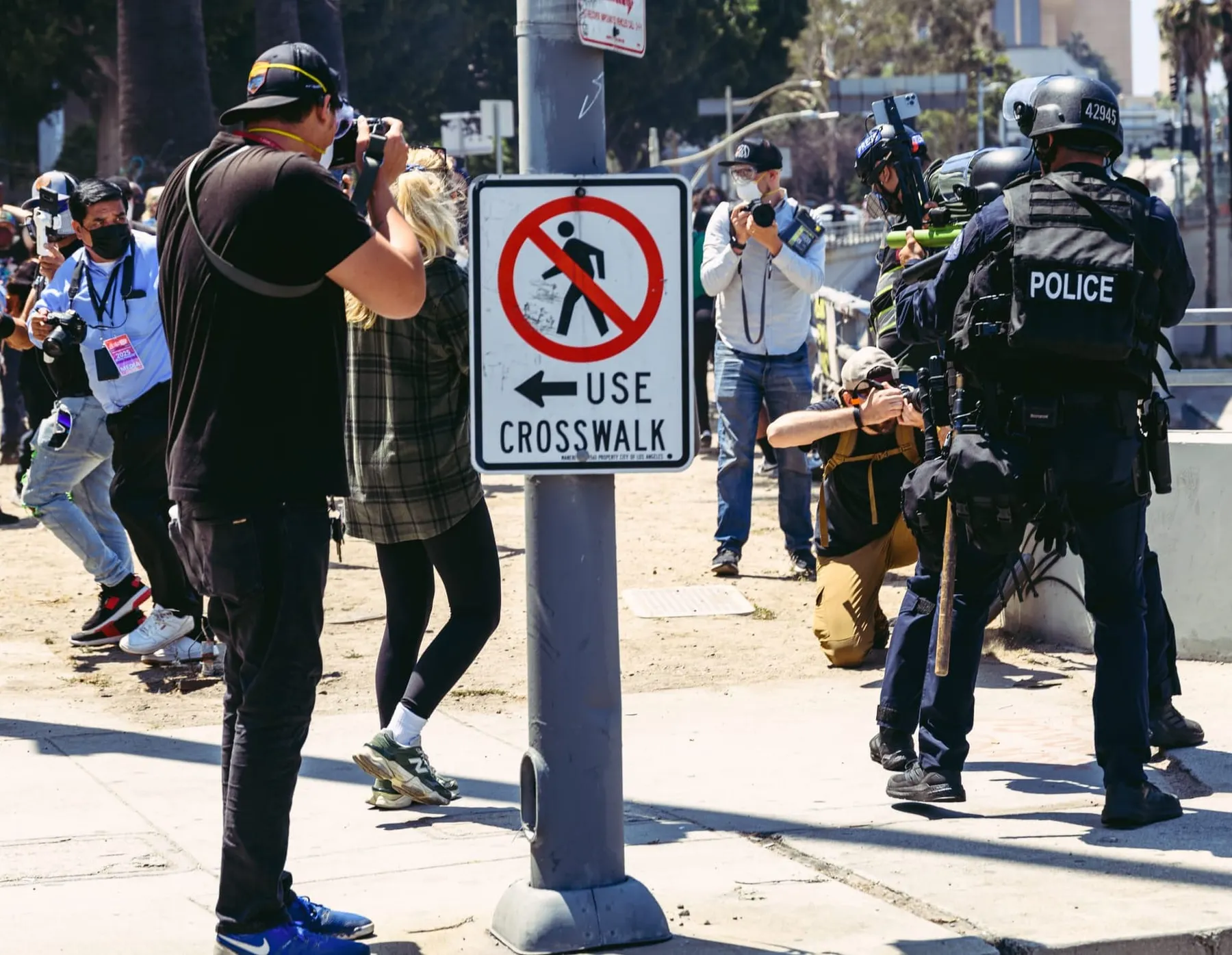 People, including journalists, flee as police officers in riot gear point guns at them.