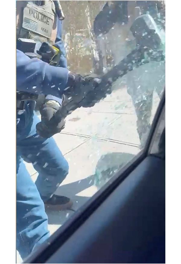 A police officer smashes the window of a car with a metal pick to remove an undocumented person from their car. 