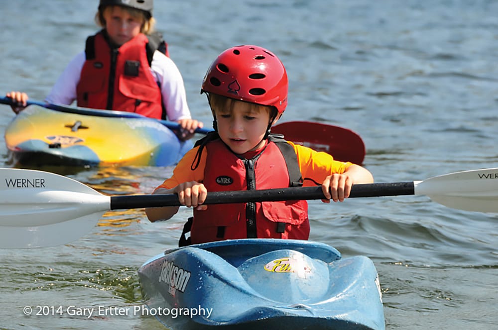 Picture of two kids kayaking on a river. 