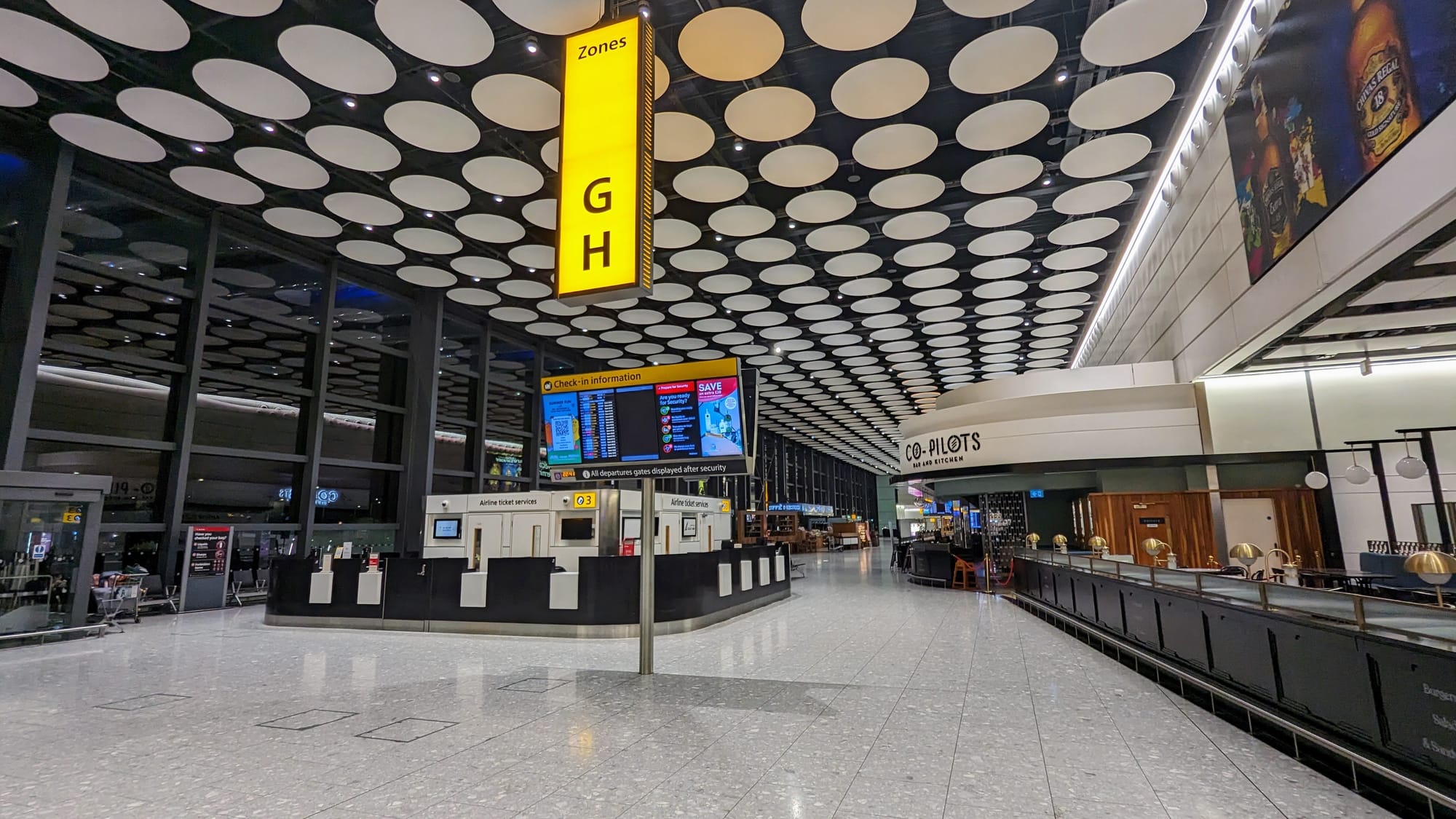 The check-in concourse at Heathrow Terminal 4, with yellow wayfinding signs and a patterned ceiling.